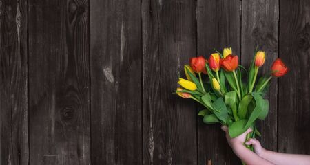 The spring sale. A bouquet of fresh red and yellow tulips in the girl 's hand on a rustic wooden background.Mothers and women's day.Spring festival.Banner for a store or website.Zero Waste.Copy space.の写真素材
