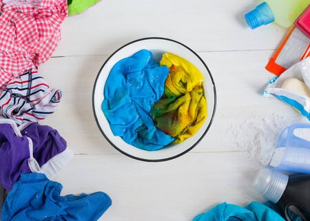 Dirty kids clothing is scattered and soaked in soapy water on a white wooden tableの写真素材