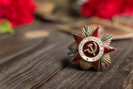 Victory Day.Selective focus on the Order of the red star with the Russian inscription Patriotic war on a wooden background with red carnations.Celebration on may 9.Memorial day.Greeting card.の写真素材