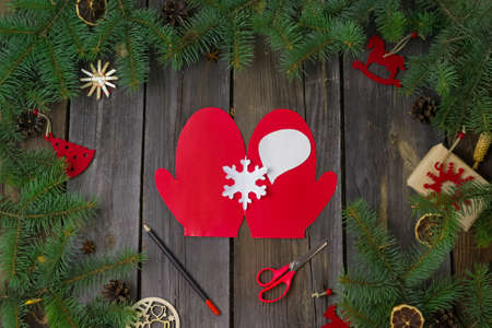 DIY Christmas and happy New year greeting card.On a wooden table with tree branches,red paper mitten with a white snowflake.Christmas instructions.decorations.Gifts.Step by step.Flat lay.Top viewの写真素材