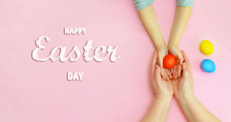 Happy Easter day.A little girl and her mother are holding colorful eggs on a pink background.A...