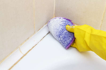 A woman's hand in a yellow glove cleans the tiles in the bathroom with detergent.Cleaning the...