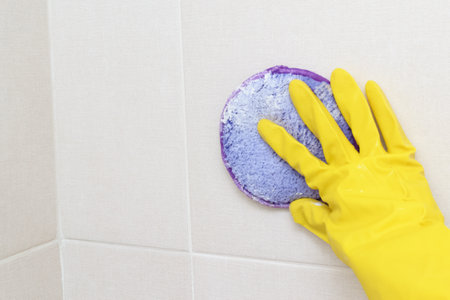 A woman's hand in a yellow glove cleans the tiles in the bathroom with detergent.Cleaning the house.Cleaning of dirty plaque.の写真素材