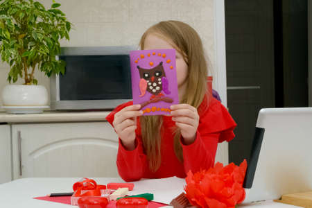 Little blonde girl makes Mother's Day or birthday greeting card and holds a gift in his hands. DIY...