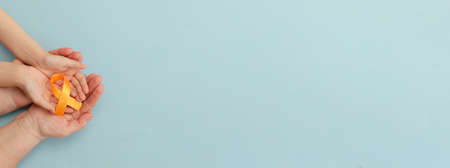 Hands of mother and child hold orange ribbon on blue background.Concept. World Multiple Sclerosis day.Layout. Copy space. Banner. Mock up.の写真素材