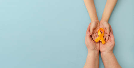 Hands of mother and child hold orange ribbon on blue background.Concept. World Multiple Sclerosis day.Layout. Copy space. Banner. Mock up.の写真素材