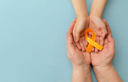 Hands of mother and child hold orange ribbon on blue background close up.Concept. World Multiple Sclerosis day.Layout. Copy space. Banner. Mock up.の写真素材