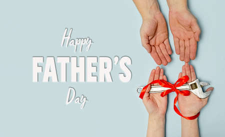 Happy father's day. Greeting card. Gift wrench with a red ribbon in hands of daughter and father on blue background. Banner for the sale in store, website. Vatertag. Layout. Top viewの写真素材