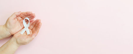 Hand women holding white ribbon on light pink background.Concept lung cancer awareness November month. Banner. Top view. Copy space. Mock up.の写真素材