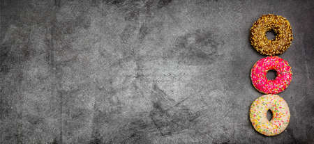 International World Donut Day. Delicious sweet donuts with icing and filling inside on a dark background. American favorite baked goods. Greeting card or banner for a website or store sale. copy spaceの写真素材