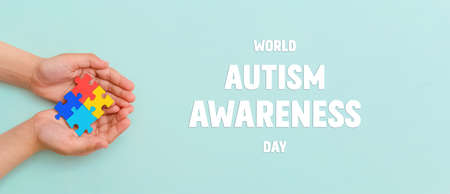 World autism awareness day. Hands of small child holding colorful puzzles on blue background.Concept - Autistic Pride Day. Banner. Top view. Layoutの写真素材