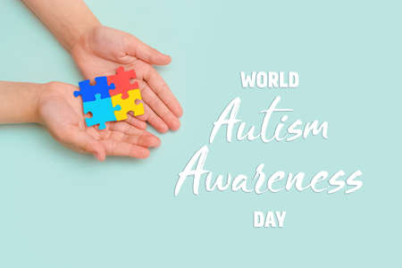 World autism awareness day. Hands of small child holding colorful puzzles on blue background.Concept...