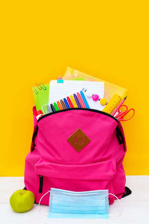 Back to school. Backpack for school with bright colorful office supplies and medical mask on yellow background. Stationery for school children's studies. Greeting card or banner for sale. Verticallyの写真素材