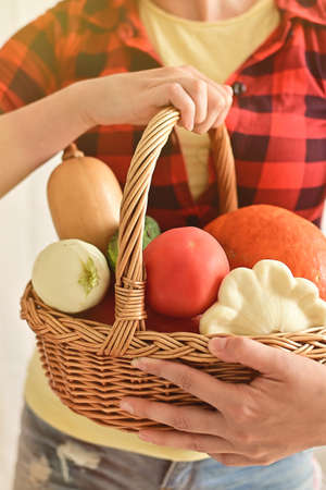 A woman holds a basket with ripe pumpkins, tomatoes,squash and zucchini in close-up. Soft focus. Autumn vegetables. Harvest festival. verticalの写真素材