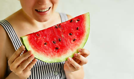 The hands of a young woman hold a piece of ripe juicy watermelon on a light background. The taste of...