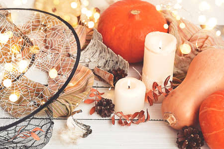 Halloween or Thanksgiving day. Ripe orange pumpkins next to bright garlands, leaves, cones from autumn garden. Magic candles and witch hat for festive party. Occultism and divination. Greating cardの写真素材
