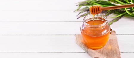 Fresh honey in a glass jar on white table. Wooden spoon with dripping honey. World Bee and Honey Day. Beekeeping. Healthy foodの写真素材