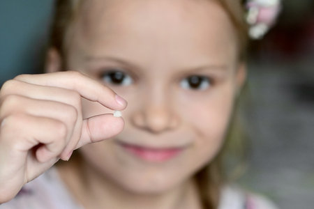 Close up of a little girl holding a fallen milk tooth in her hand. Problems with teeth. Pediatric dentistryの写真素材