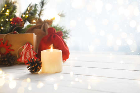 Merry Christmas. Christmas candle and gifts on a white wooden table next to branches of a Christmas tree and shining lights. Advent. Greeting card or banner for website. copy space