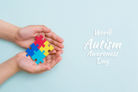 World autism awareness day. The hands of a small child close up holding colorful puzzles on blue background. Bannerの写真素材