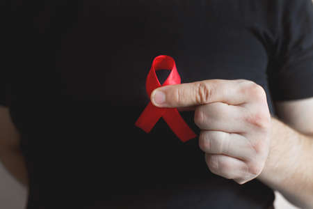 Concept World AIDS and hiv day. A man in a black T-shirt holds a red ribbon on a white background. Blood transfusion and donation. Hemophilia day. World Health Day.Copy space. Banner. close-upの写真素材