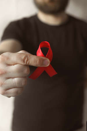 Concept World AIDS and hiv day. A man in a black T-shirt holds a red ribbon on a white background. Blood transfusion and donation. Hemophilia day. World Health Day. verticallyの写真素材