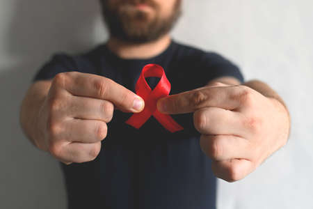 Concept World AIDS and hiv day. A man in a black T-shirt holds a red ribbon on a white background. Blood transfusion and donation. Hemophilia day. World Health Day Banner close-up.の写真素材