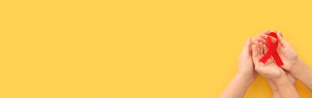Concept World AIDS Day. Hands of woman holding red ribbon on yellow background. Blood transfusion and donation. Hemophilia day. World Health Day. Layout. Copy space. Banner. top viewの写真素材