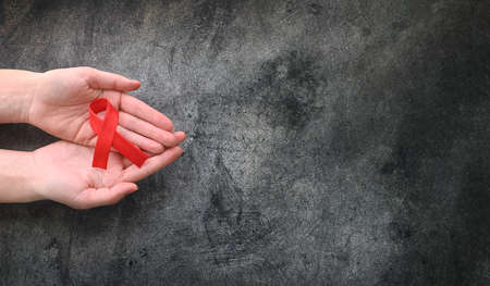 Concept World AIDS Day. Hands of woman holding red ribbon on black background. Blood transfusion and donation. Hemophilia day. World Health Day. top view. Copy space. Banner.の写真素材