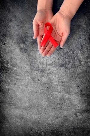 Concept World AIDS Day. Hands of woman holding red ribbon on black background. Blood transfusion and donation. Hemophilia day. World Health Day. Layout. Copy space. Bannerの写真素材
