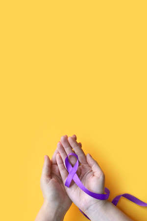 International Epilepsy Day. Adult hands holding purple ribbon on yellow background. Alzheimer's disease, Pancreatic cancer, Hodgkin's Lymphoma awareness. World Lupus Day and world cancer. verticallyの写真素材