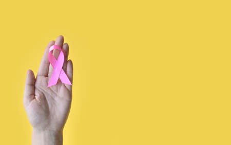 Breast Cancer Awareness. Hand of woman holding pink ribbon on yellow background. World cancer day. National cancer survivor day. Concept I Am and I Will. copy spaceの写真素材