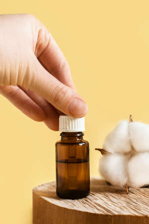 Woman's hand holds cosmetic product with essential oil, Vitamin and prebiotic serums in glass bottle for care of hair and skin of face on beige background next to natural ingredients. verticalの写真素材