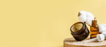 Glass cosmetic bottle or essential oil with Vitamin and prebiotic serums. Cosmetics in jar for care of hair and skin of face, body on beige background next to natural ingredients. banner. copyspaceの写真素材