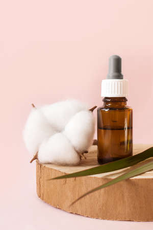 Glass cosmetic bottle or essential oil with Vitamin and prebiotic serums for care of hair and skin of face, body on pink background next to natural ingredient. copyspace. verticalの写真素材