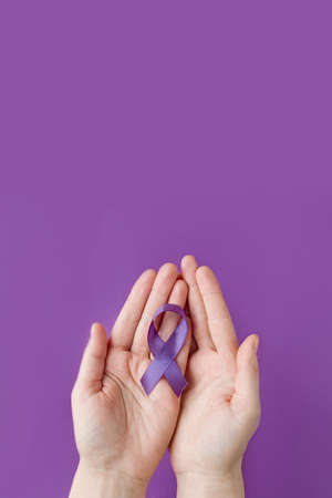 International Epilepsy Day. Adult hands holding purple ribbon on purple background. Alzheimer's disease, Pancreatic cancer, Hodgkin's Lymphoma awareness. World Lupus Day and world cancer. verticallyの写真素材