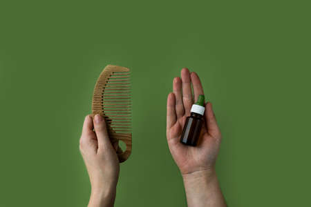 Women's hands hold a natural wooden comb and a bottle with essence, vitamins and a prebiotic for...