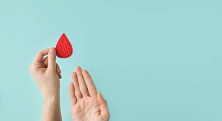 Concept of give blood donation, blood transfusion. Hands woman hold drop of blood on blue background. World hemophilia day. World AIDS and hiv day. copyspace. top view bannerの写真素材