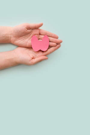World Thyroid Day. Womens hands hold a paper form of the thyroid gland on a blue background....