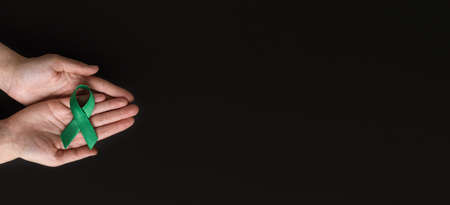 world bipolar day. Adult hands holding green ribbon on black background. Mental health awareness day, Depression, Cerebral palsy. world kidney day. top view. copy spaceの写真素材