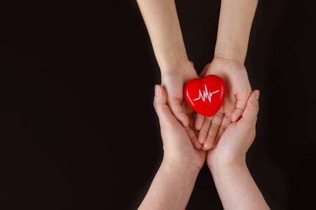 World Hypertension Day. Adult and child holding red heart with a heartbeat chart with his hands - a symbol of high blood pressure. World heart day, world health day. copy spaceの写真素材