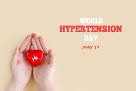 World Hypertension Day. Women's hands hold red heart with heartbeat chart - a symbol of high blood pressure. Hypertension Day in May 17th. world heart day.の写真素材