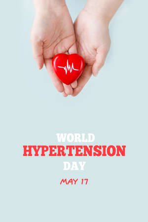 World Hypertension Day. Women's hands hold red heart with heartbeat chart - a symbol of high blood pressure. Hypertension Day in May 17th. world heart day. vertical photoの写真素材