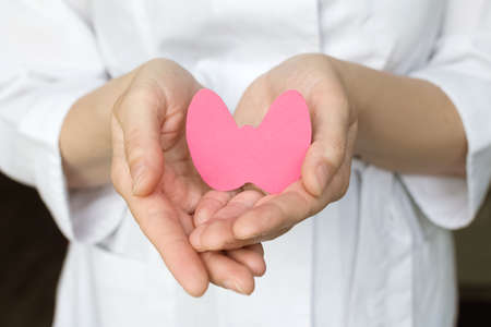 World Thyroid Day. Womens hands hold a paper form of the thyroid gland on a blue background....