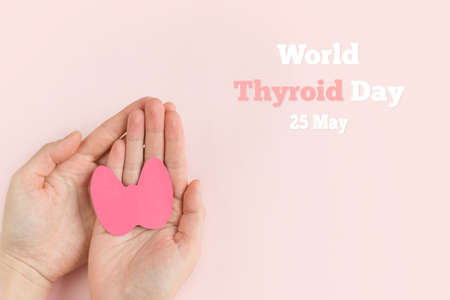World Thyroid Day. Womens hands hold paper form of the thyroid gland on pink background. Problems with thyroid. Polycystic disease. World cancer dayの写真素材