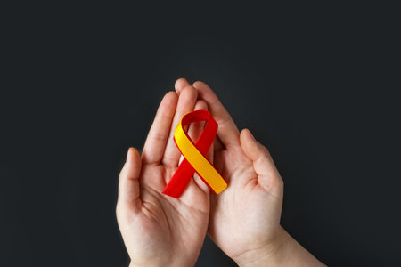world hepatitis day. Adult hands holding red yellow ribbon on black background. Awareness of prevention and treatment of viral hepatitis. Liver cancer. world cancer day. copyspace. banner.の写真素材