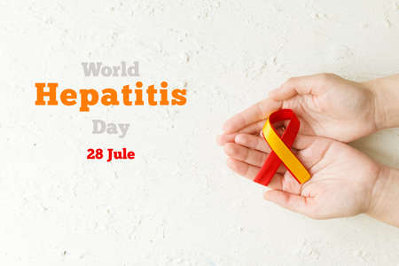 world hepatitis day. Adult hands holding red yellow ribbon on white background. Awareness of...