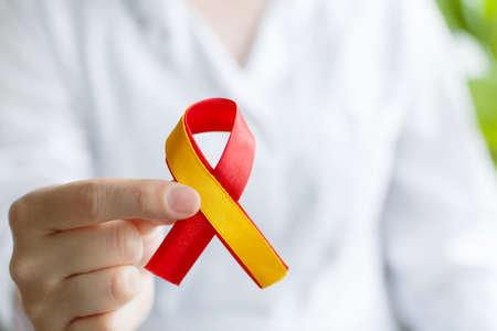 world hepatitis day. Doctor woman holding red yellow ribbon in her hands. Awareness of prevention and treatment of viral hepatitis. Liver cancer. world cancer day. banner. close upの写真素材