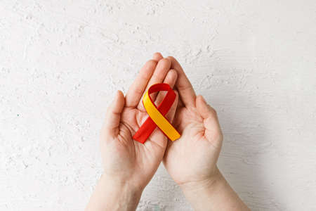 world hepatitis day. Adult hands holding red yellow ribbon on white background. Awareness of prevention and treatment of viral hepatitis. close-up. Liver cancer. world cancer day. banner.の写真素材