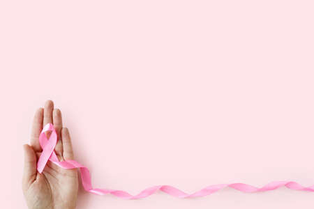 Breast Cancer Awareness Month. Woman hand holding pink ribbon on pink background. International symbol of Breast Cancer in October. health care and medicine concept. copyspace.の写真素材